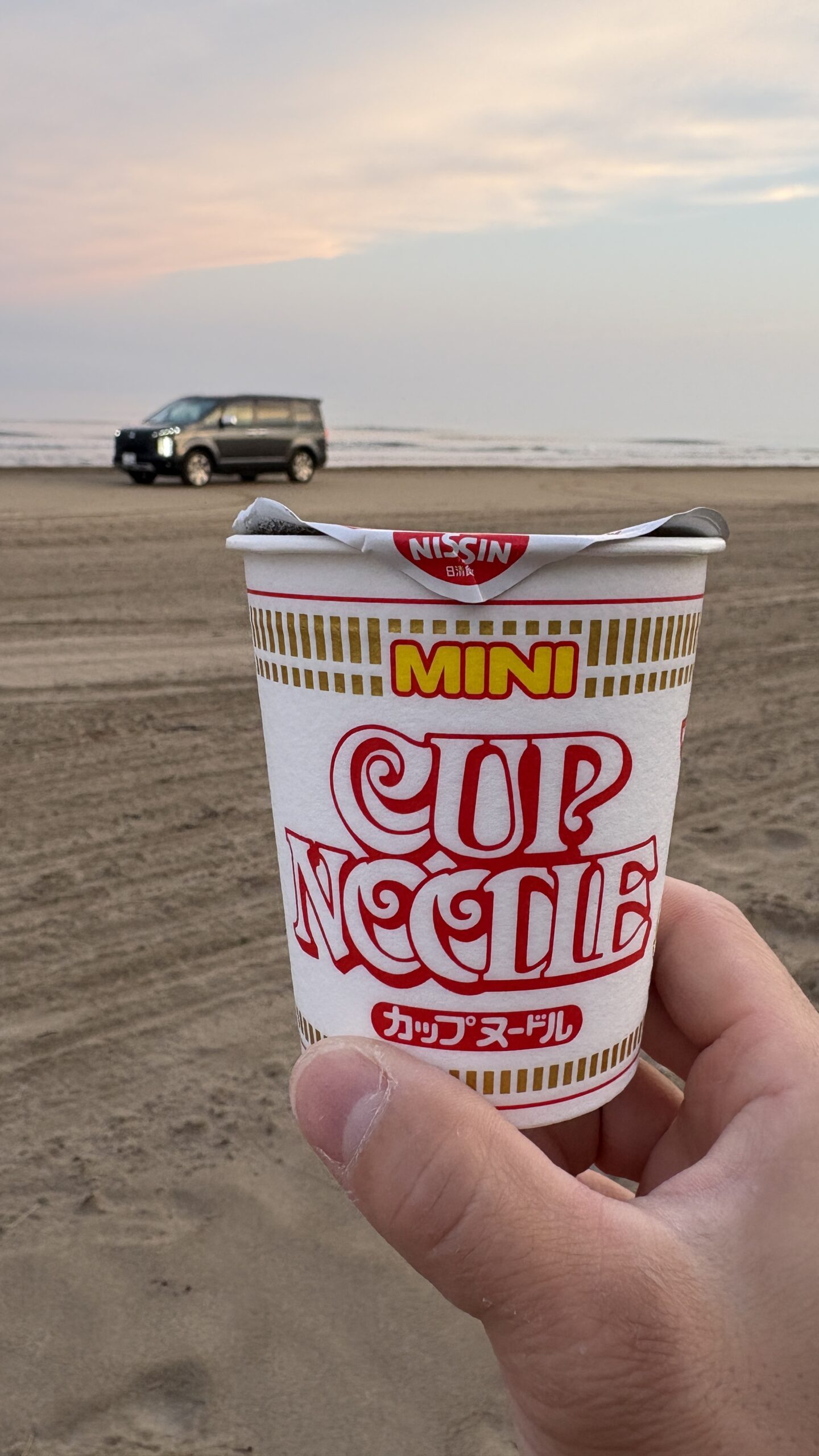カップヌードル越しに見えるデリカD:5と朝焼けの海